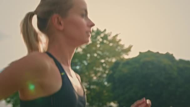 Sportowiec dziewczyna w czarnej odzieży sportowej jogging intensywny sprint działa na świeżym powietrzu trening w promieniach porannego wschodu słońca. Widok z boku blondynka sportowiec biegacz praktykujący cardio do zawodów wyścigowych lub maraton - Materiał filmowy, wideo