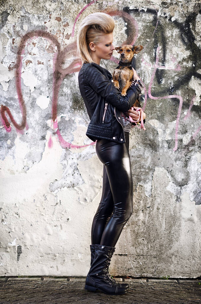 Até os rockstars precisam de um melhor amigo. Uma jovem mulher na moda segurando um pequeno cão em um ambiente urbano - Foto, Imagem
