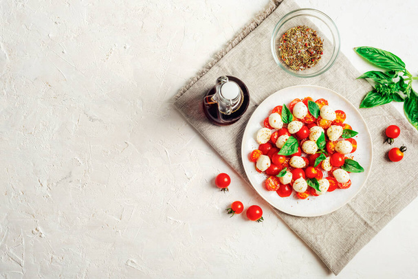 Insalata caprese italiana con pomodorini, mozzarella, basilico, salsa balsamica su un tavolo bianco. Vista dall'alto, disposizione piatta, spazio di copia. - Foto, immagini