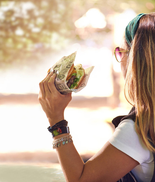 Ώρα για λίγο νόστιμο. Μια νεαρή γυναίκα τρώει ένα χάμπουργκερ έξω. - Φωτογραφία, εικόνα