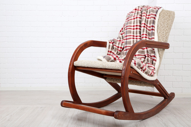 Comfortable rocking-chair with rug on wooden floor near the brick wall background - Photo, image