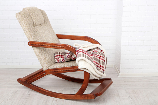 Comfortable rocking-chair with rug on wooden floor near the brick wall background - Photo, image