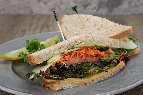 Sanduíche de escolha Vegan com cenouras desfiadas, abacate, tomate, alface e pepino entre dois pedaços de torrada de trigo mel. - Foto, Imagem