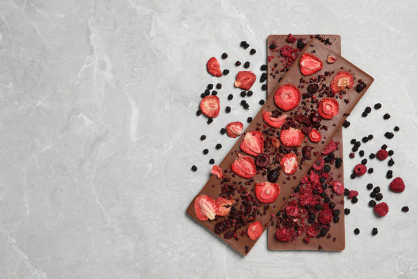 Chocolate bars with freeze dried berries on grey marble table, flat lay Space for text - Photo, image