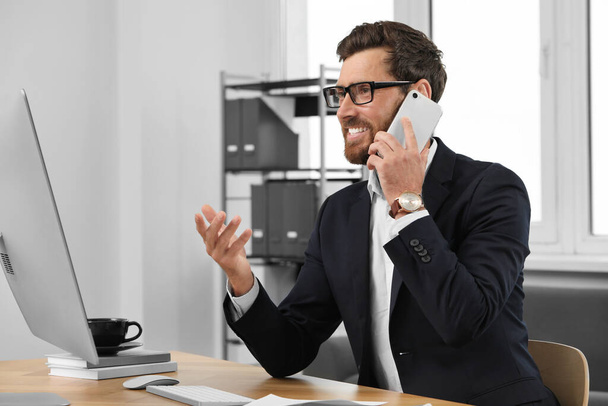 Happy bearded man talking on smartphone in office - Фото, изображение