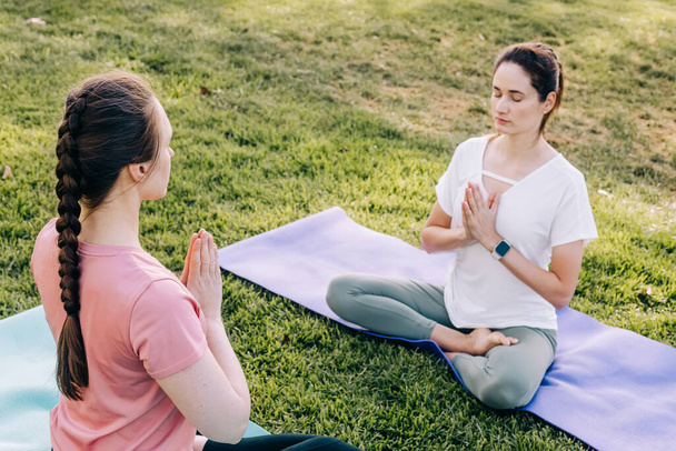 Two young women in the park doing yoga. Exercising outdoors, healthy lifestyle - Photo, Image
