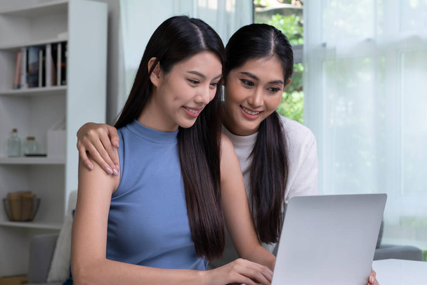 Красивая молодая азиатская лесбийская пара, общающаяся онлайн на ноутбуке. ЛГБТ-лесбиянки вместе смотрят вебинар фильмов на ноутбуке, изучают электронное обучение, делают бумажную работу, оплачивают счета в домашнем офисе - Фото, изображение
