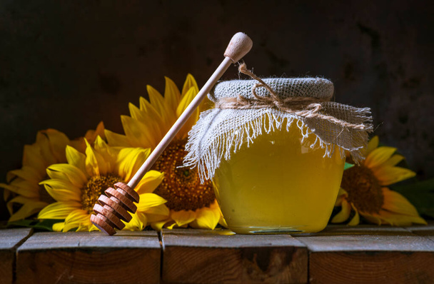 Biologische zonnebloem honing in een transparante pot met een jute zak servet deksel dipper concept van gezond eten, oude houten achtergrond Pot stilleven donker voedsel glazen schaal - Foto, afbeelding