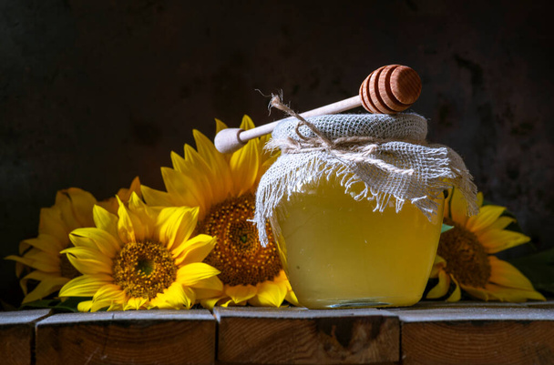 Organic sunflower honey in a transparent jar with a burlap sack napkin lid dipper concept of healthy eating, old wooden background Pot still life dark  food glass bowl - Foto, afbeelding