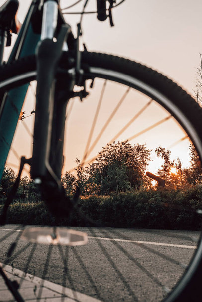 Bike at the summer sunset on the tiled road in the city park. Cycle closeup wheel on blurred summer background. Cycling down the street to work at summer sunset. Bicycle and ecology lifestyle concept. - Photo, Image