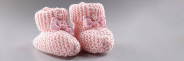 Close-up of pair of knitted pink baby booties with cute bow on it. Handicraft shoes for newborn baby on grey surface. Handmade, crochet, wool, care concept - Photo, Image