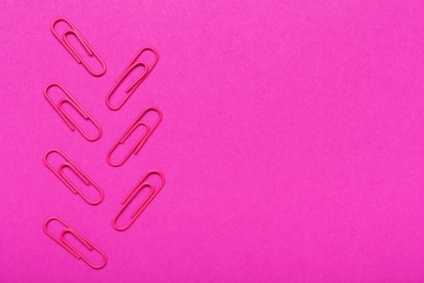 siete clips de papelería roja dispuestos sobre fondo lila, con espacio para copias, concepto de oficina, disposición plana - Foto, imagen