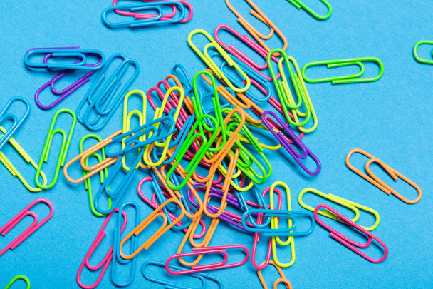 many multicolored paper clips scattered over a blue background, concept, flat lay - Foto, immagini
