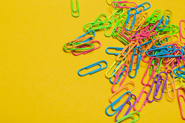 a lot of multicolored paper clips scattered on a yellow background, office concept, copy space - Fotoğraf, Görsel
