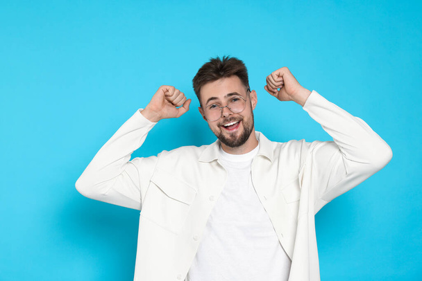Excited man in white jacket celebrating victory on light blue background - Фото, изображение