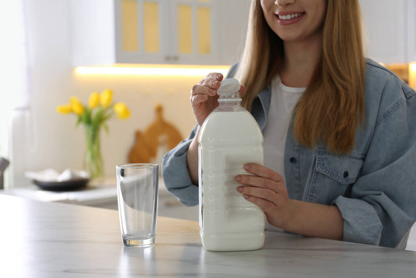 Young woman with gallon bottle of milk at white marble table in kitchen, closeup - Foto, Imagem
