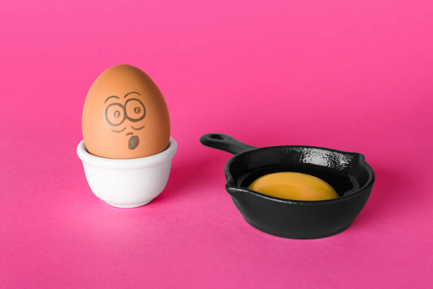 Egg with drawn shocked face and yolk in small frying pan on pink background - Foto, Imagem