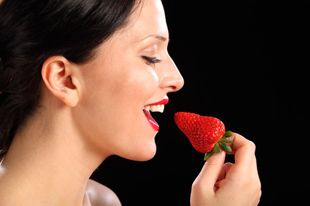 Beautiful happy woman eating red strawberry fruit - 写真・画像