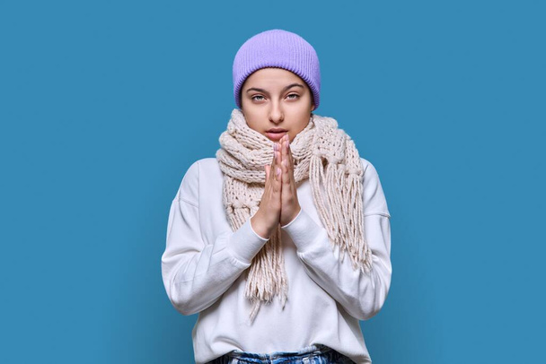 Winter headshot portrait of young female in hat sweater scarf. Adorable beautiful cute teenage girl looking at camera on blue studio background. Cold season New Year Christmas holidays fashion beauty - Φωτογραφία, εικόνα