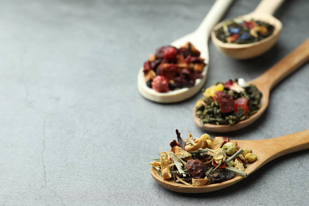 Different kinds of dry herbal tea in wooden spoons on light grey table, closeup. Space for text - Foto, imagen