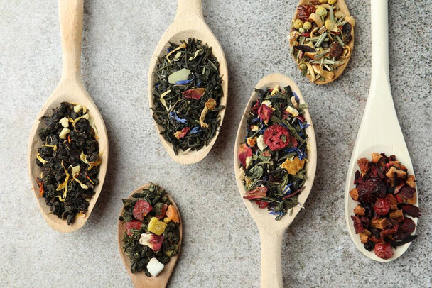 Different kinds of dry herbal tea in wooden spoons on light grey table, flat lay - Valokuva, kuva