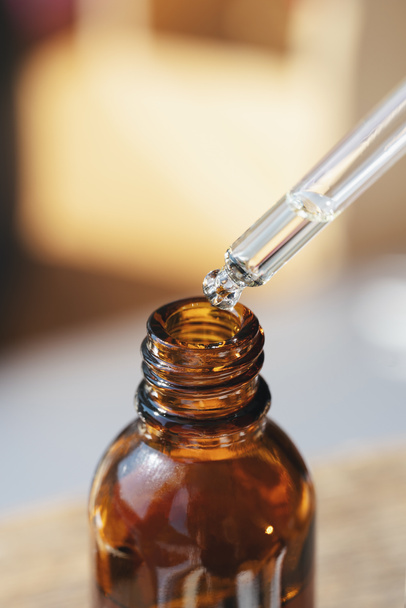Open amber bottle with dropper pipette with serum or essential oil. Skincare products, natural cosmetic on blurred background. Medicine and beauty concept for face care. Selective focus in the center - 写真・画像