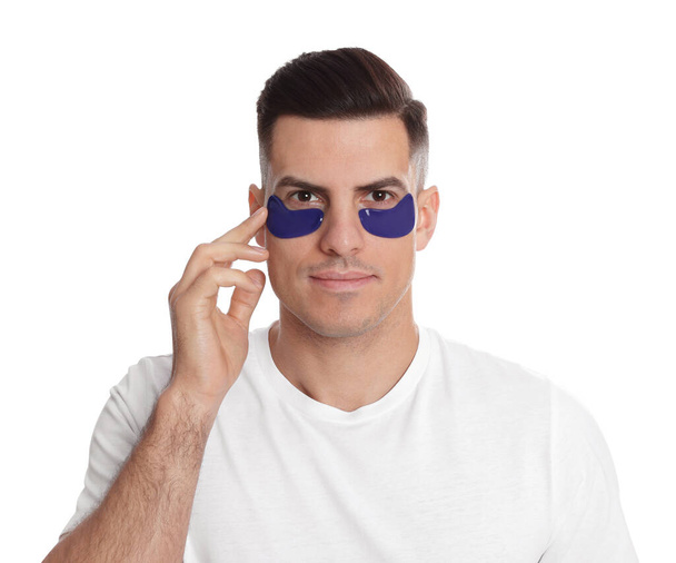 Man applying blue under eye patch on white background - Фото, изображение