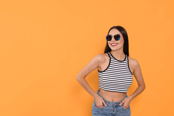 Attractive happy woman in fashionable sunglasses against orange background. Space for text - Фото, изображение