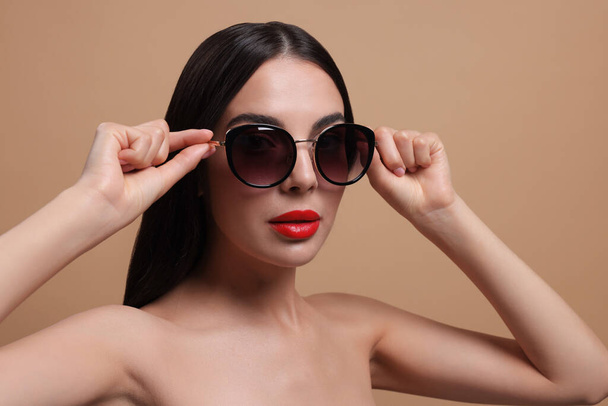 Attractive woman wearing fashionable sunglasses against beige background - Valokuva, kuva