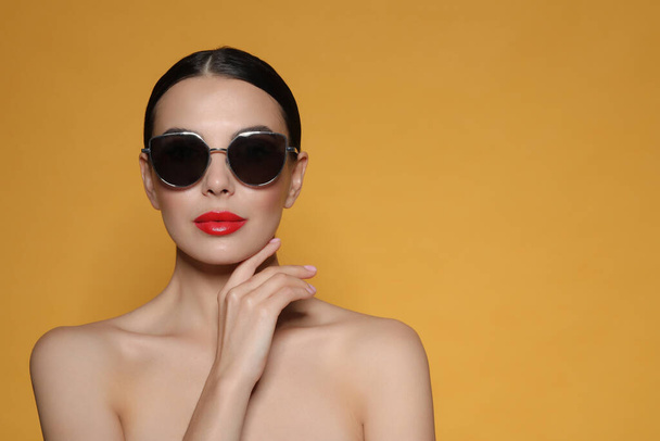 Attractive woman in fashionable sunglasses against orange background. Space for text - Fotó, kép