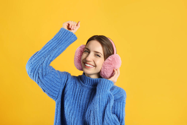 Happy woman wearing warm earmuffs on yellow background - Fotó, kép