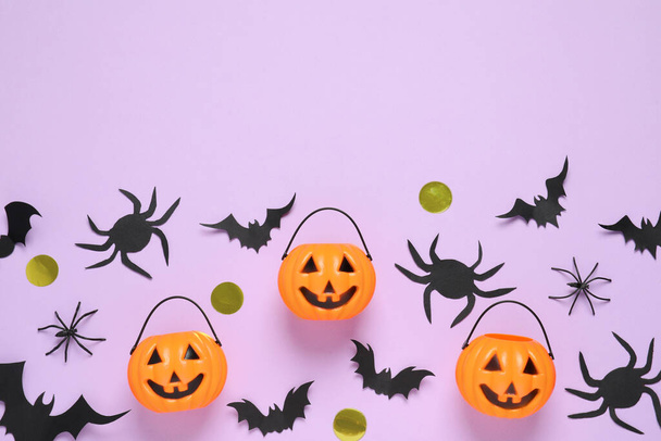 Flat lay composition with paper bats, plastic pumpkin baskets and spiders on light violet background, space for text. Halloween decor - Photo, Image