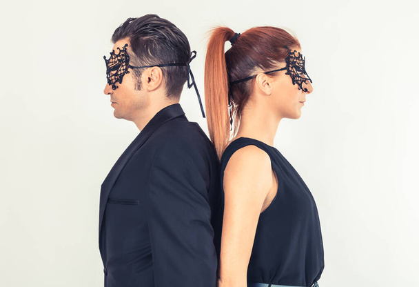 Vista lateral de una pareja con máscaras en las caras de pie espalda con espalda. - Foto, Imagen
