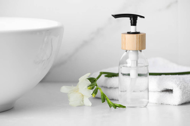Bottle with dispenser cap, towel and beautiful flower on white table in bathroom, closeup - Photo, Image