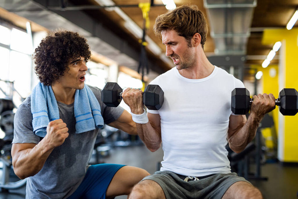 Fitness, sport, exercising and diet concept. Happy fit man exercising together with his personal trainer, friend in gym. - Photo, Image
