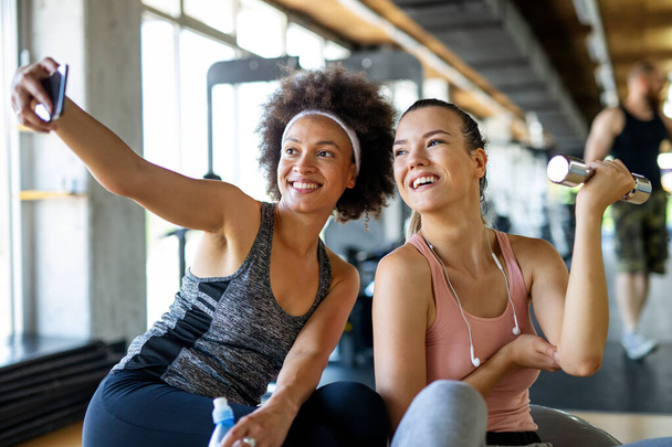 Happy fit women, friends smiling, talking and taking photos after work out in gym. Social media, people, sport concept. - Photo, Image