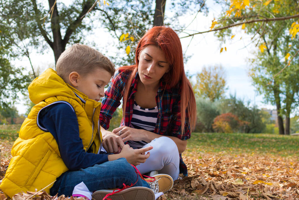 Молодая мать и ее сын отдыхают на осенних листьях и смотрят что-то по мобильному телефону.  - Фото, изображение