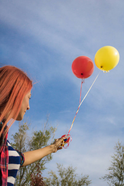 Niski kąt widzenia kobiety trzymającej czerwone i żółte balony na niebie w parku. - Zdjęcie, obraz