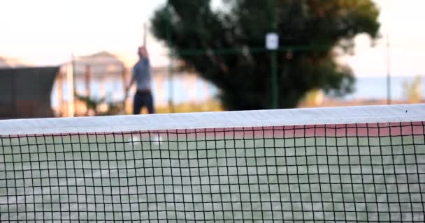 Mann im Tennistraining schlägt Ball auf Tennisplatz. Tennistraining im Freien durch Netz - Filmmaterial, Video
