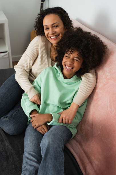 high angle view of happy african american mother hugging smiling preteen daughter in living room - Fotografie, Obrázek