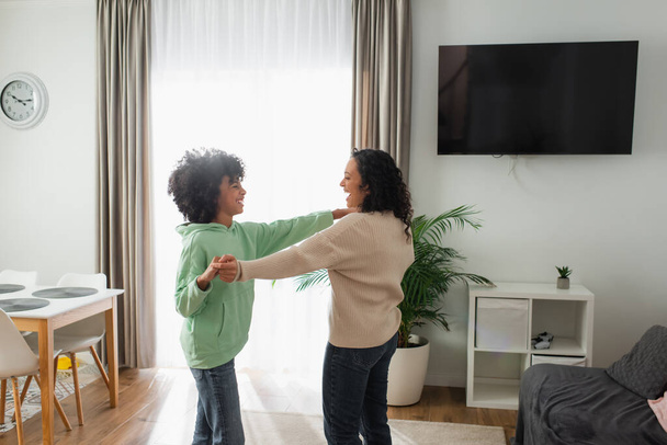 cheerful african american woman holding hands while dancing with preteen daughter  - Fotografie, Obrázek