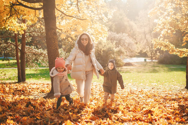 Happy mother with two little kids running in the beautiful sunny autumn park. Family having fun together outside. - Fotoğraf, Görsel