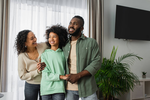 smiling african american parents hugging cheerful preteen daughter at home - Φωτογραφία, εικόνα