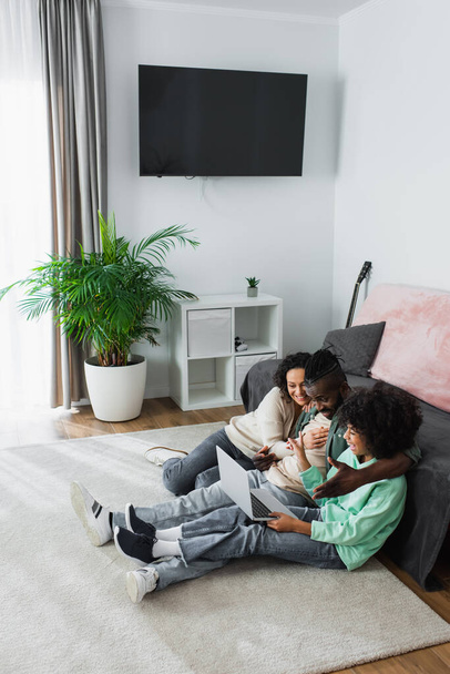 vista de ángulo alto de la alegre familia afroamericana sonriendo y viendo la película en el ordenador portátil en casa - Foto, Imagen