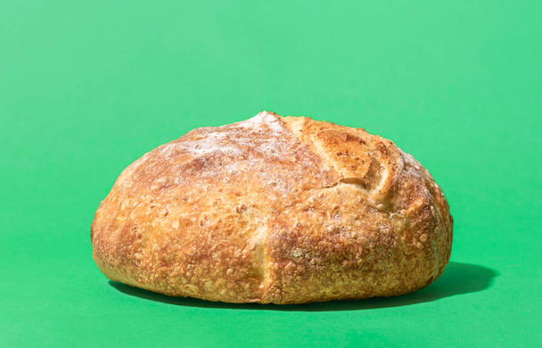 Close-up with a whole bread minimalist on a green background. Home-baked white bread in bright light. - Фото, зображення