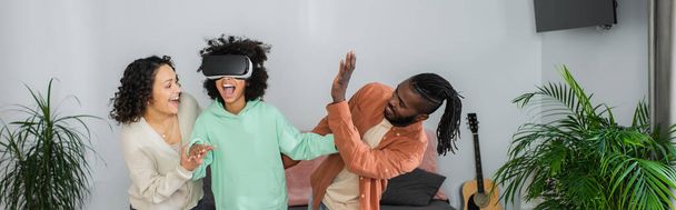 positive african american parents near preteen daughter gaming in vr headset, banner - Foto, Imagen