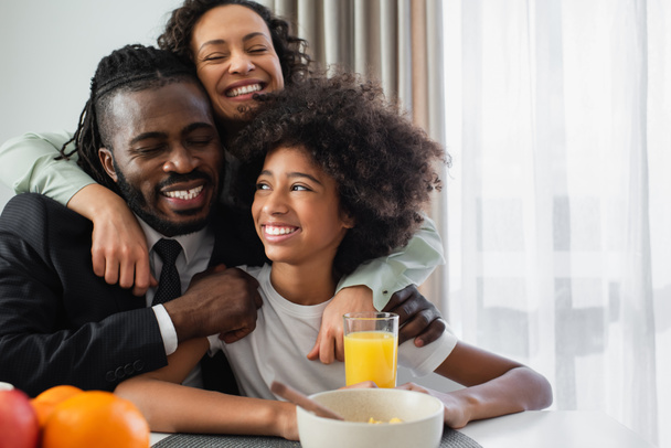 ευτυχισμένη αφροαμερικανική οικογένεια αγκαλιάζει κατά τη διάρκεια του πρωινού στο σπίτι - Φωτογραφία, εικόνα