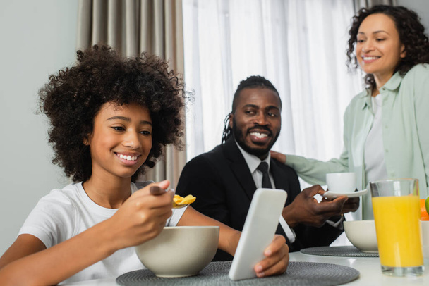 szczęśliwy Afryki dziewczyna za pomocą smartfona podczas śniadania z rodzicami  - Zdjęcie, obraz