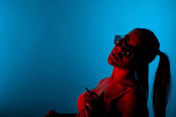 Nahaufnahme eines Silhouettenmädchens, das im Studio im Sitzen Zigarette raucht - Foto, Bild