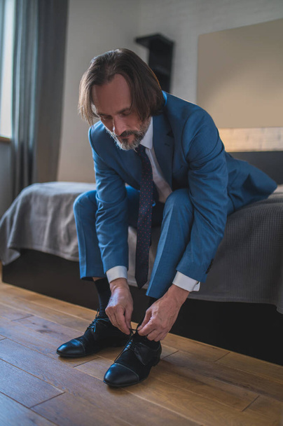 Schuhe anziehen. Mann im blauen Anzug zieht Schuhe an und sitzt auf dem Sofa - Foto, Bild